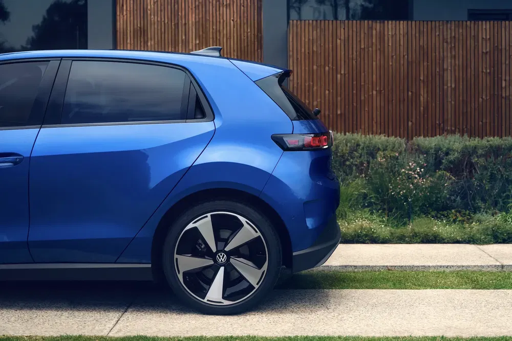 Moderne blauwe Volkswagen geparkeerd met sportvelgen, zijaanzicht bij houten muren.