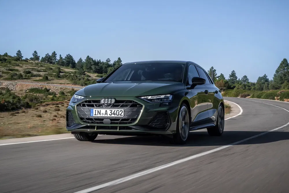 Audi A3 verte roulant sur une route sinueuse entourée de paysages boisés.