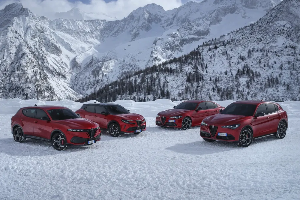 Quatre Alfa Romeo rouges sur neige avec montagnes en arrière-plan.