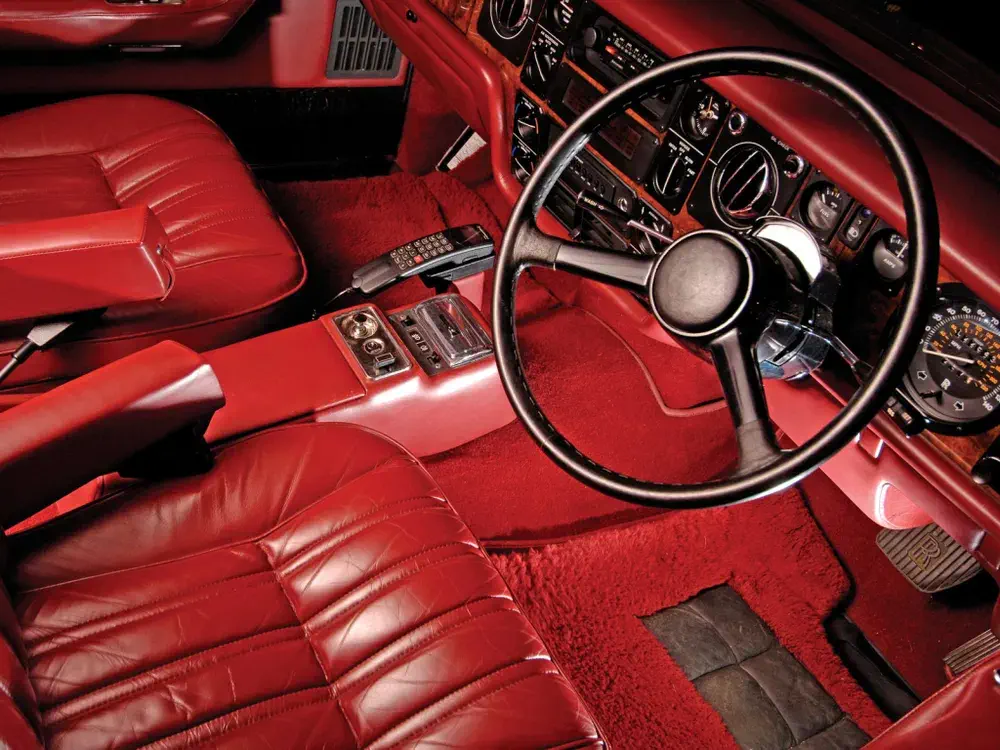 Intérieur luxueux en cuir rouge d'une voiture classique avec volant et tableau de bord vintage.
