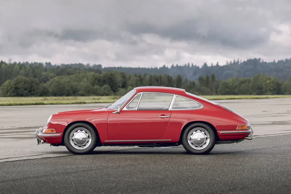 Klassieke rode Porsche 911 geparkeerd op een landingsbaan met bewolkte lucht op de achtergrond.