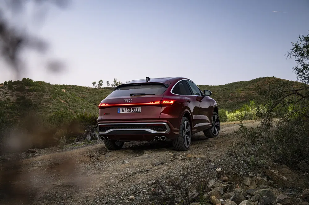 Audi Q8 rouge sur terrain rocheux avec paysage de collines verdoyantes en arrière-plan.