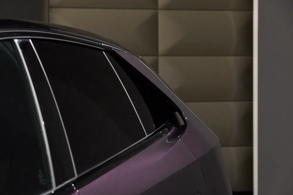 Vue latérale arrière d'une voiture électrique Tesla, couleur violet, fond matelassé moderne.