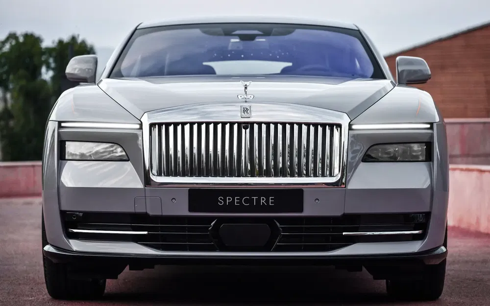 Frontale du Rolls-Royce Spectre, calandre iconique et design luxueux sur fond urbain.