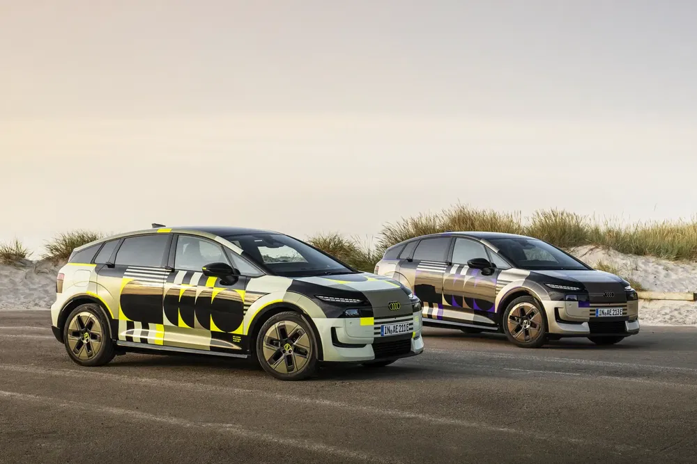 Deux Audi Q6 e-tron camouflées stationnées sur une route côtière, design avant-gardiste.