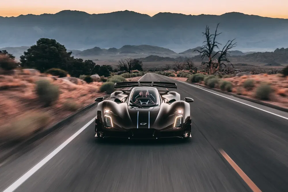 Hypercar Czinger 21C sur route montagneuse au coucher du soleil, paysage désertique.