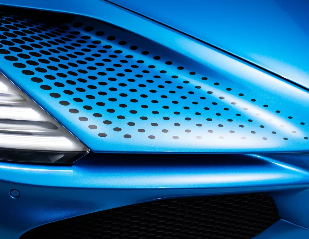 Détails du capot ventilé d'une McLaren Artura bleue, avec motifs de ventilation. Design automobile moderne.