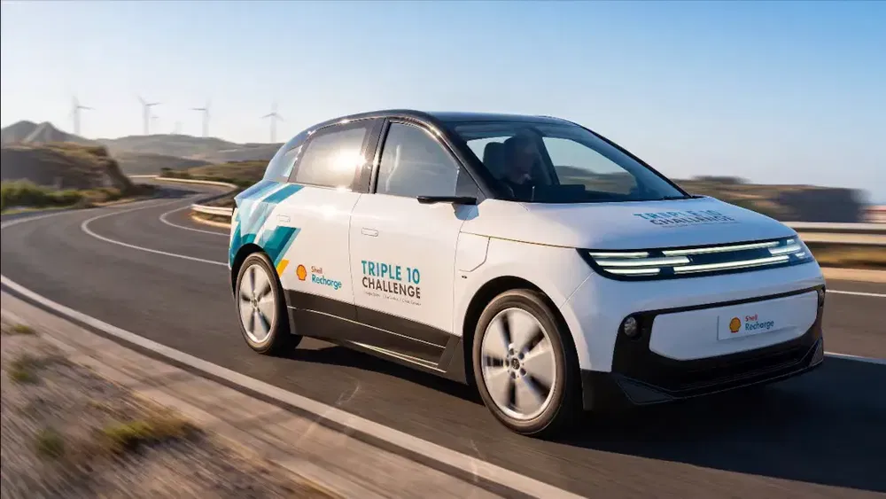 {"fr":"Voiture électrique futuriste sur route sinueuse, éoliennes en fond, Triple 10 Challenge visible.","nl":"Futuristische elektrische auto op kronkelige weg, windmolens op achtergrond, Triple 10 Challenge zichtbaar."}