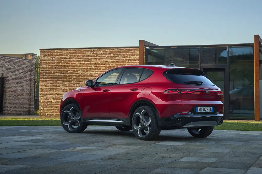 Rode Alfa Romeo Tonale SUV geparkeerd voor een modern bakstenen gebouw.
