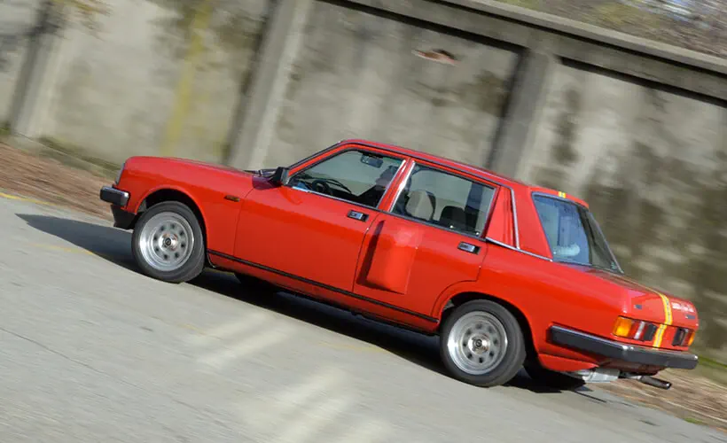 Voiture classique sport rouge avec carrosserie angulaire et jantes argentées élégantes.