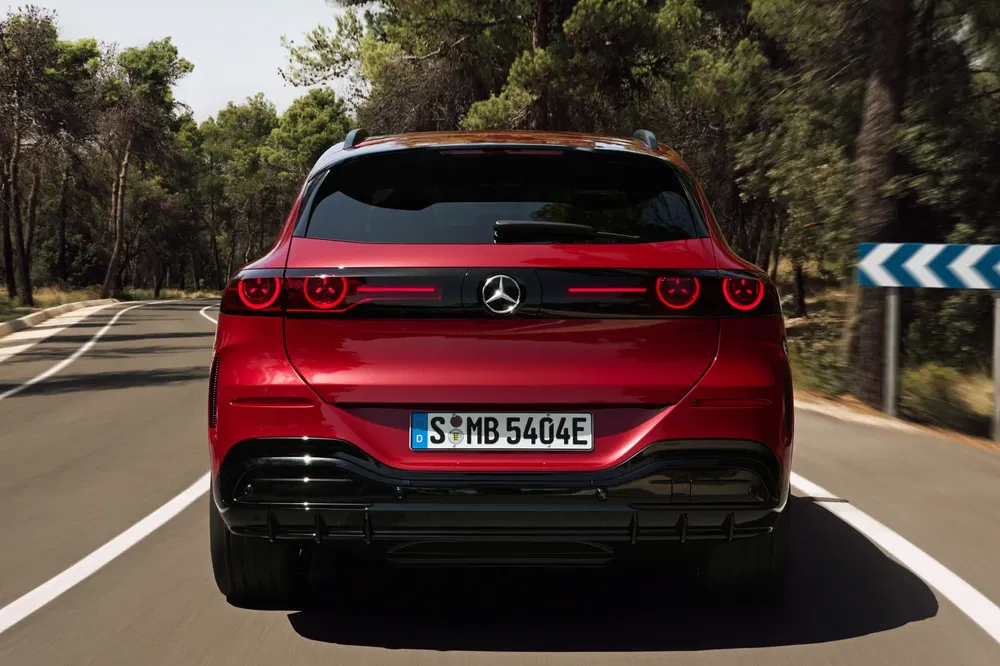 SUV rouge Mercedes-Benz EQB roulant sur une route forestière ensoleillée.
