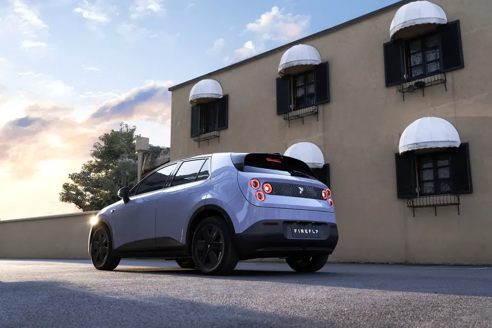 Moderne Firefly auto voor een gebouw met zwarte luiken en gedeeltelijk bewolkte lucht.