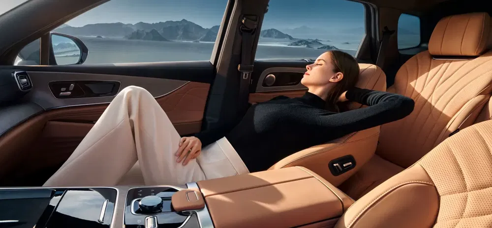 Luxe auto-interieur met beige lederen stoelen en ontspannen passagier die naar buiten kijkt.