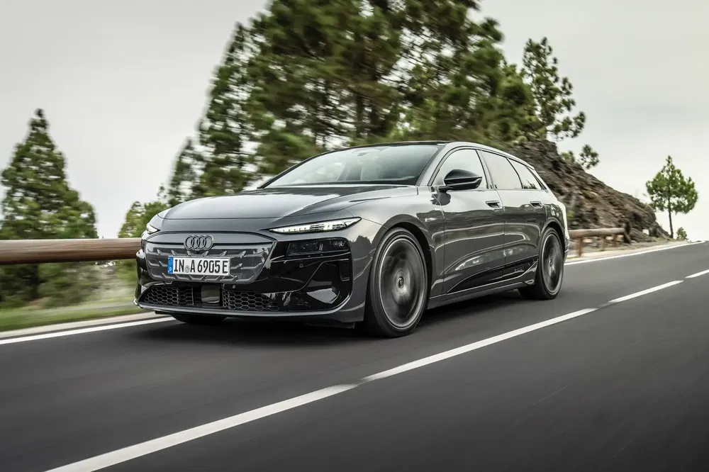 Audi e-tron GT noire, roulant sur une route bordée d'arbres, ciel nuageux.