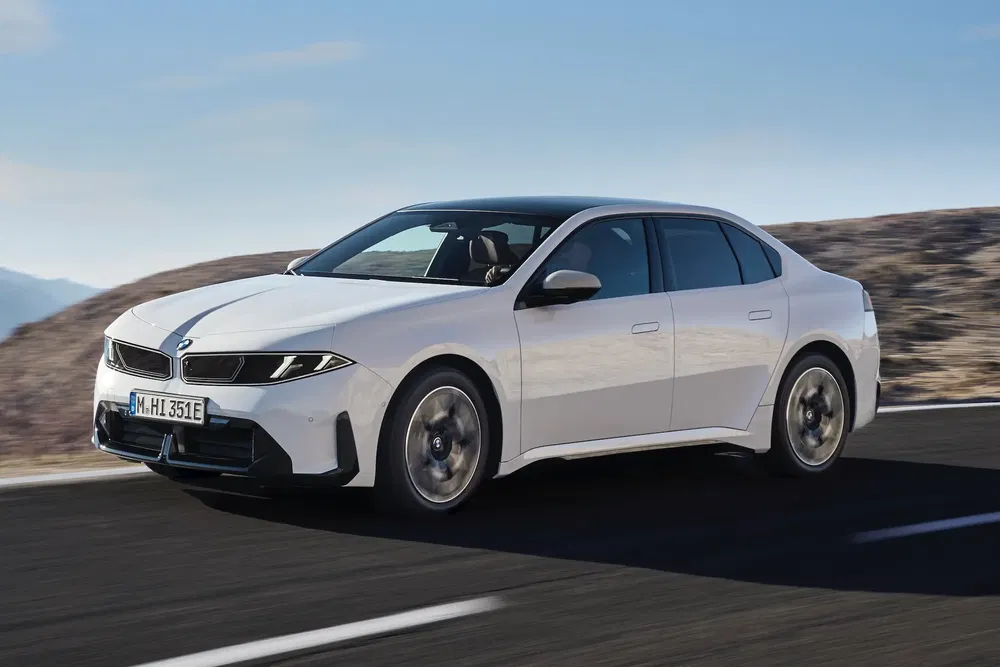 Berline BMW blanche moderne roulant sur autoroute sous ciel dégagé.