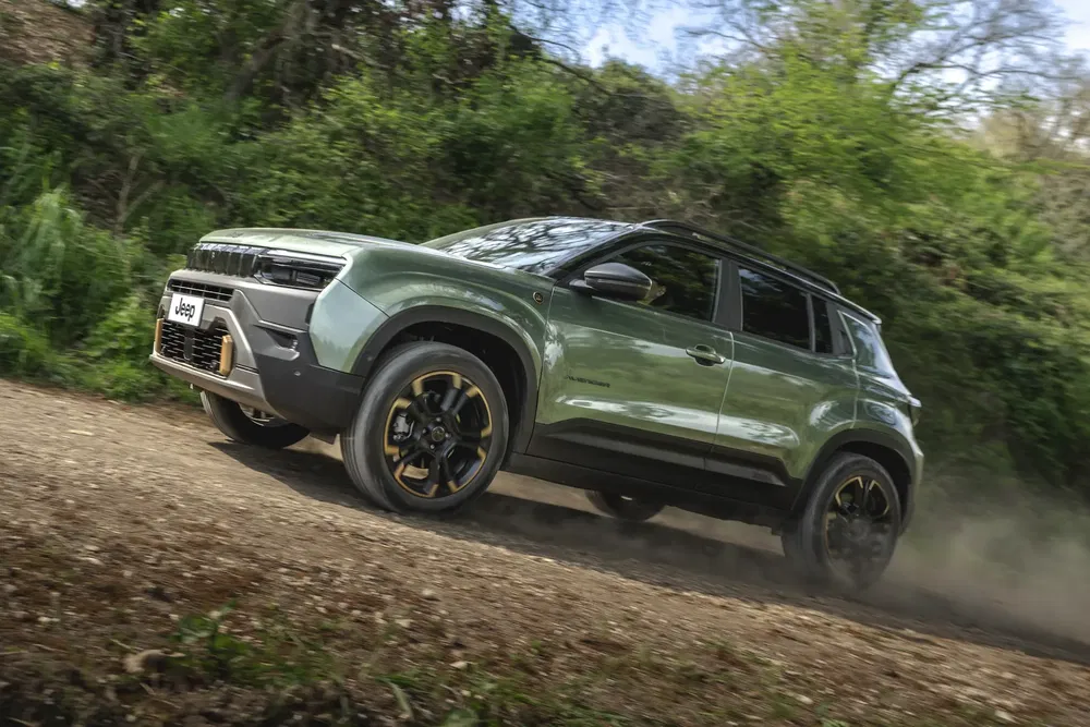 Jeep Avenger vert foncé roule sur chemin de terre en forêt.