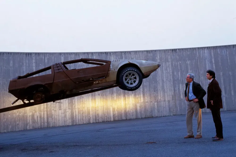 Deux hommes observent une Lamborghini antigravitationnelle près d'un mur en béton.