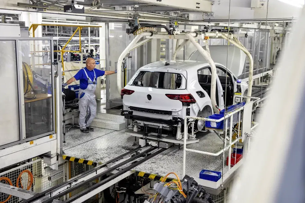 Assemblage d'une Volkswagen Golf dans une usine, supervision par un ouvrier en uniforme.