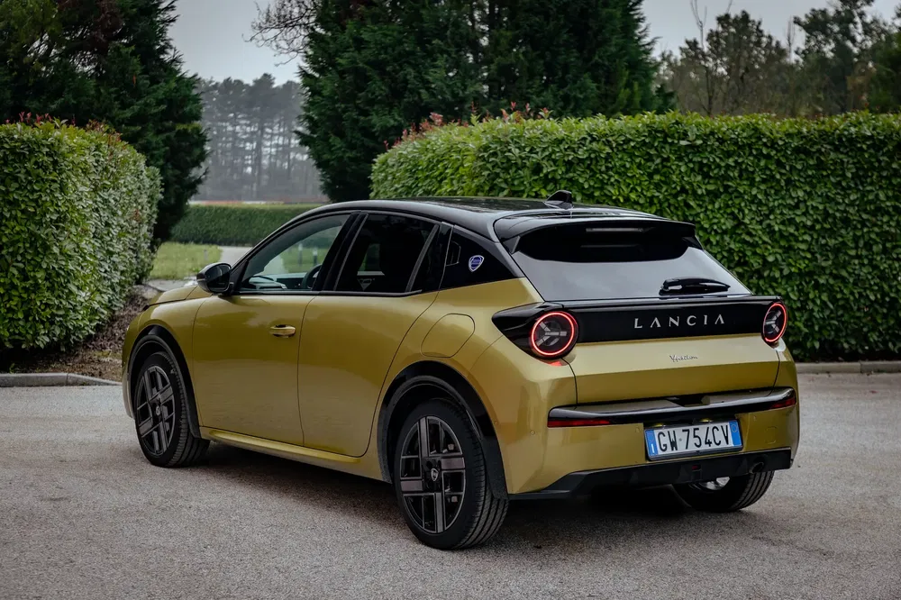Lancia compacte jaune garée, vue arrière, entourée de verdure luxuriante, plaque GW754CV.