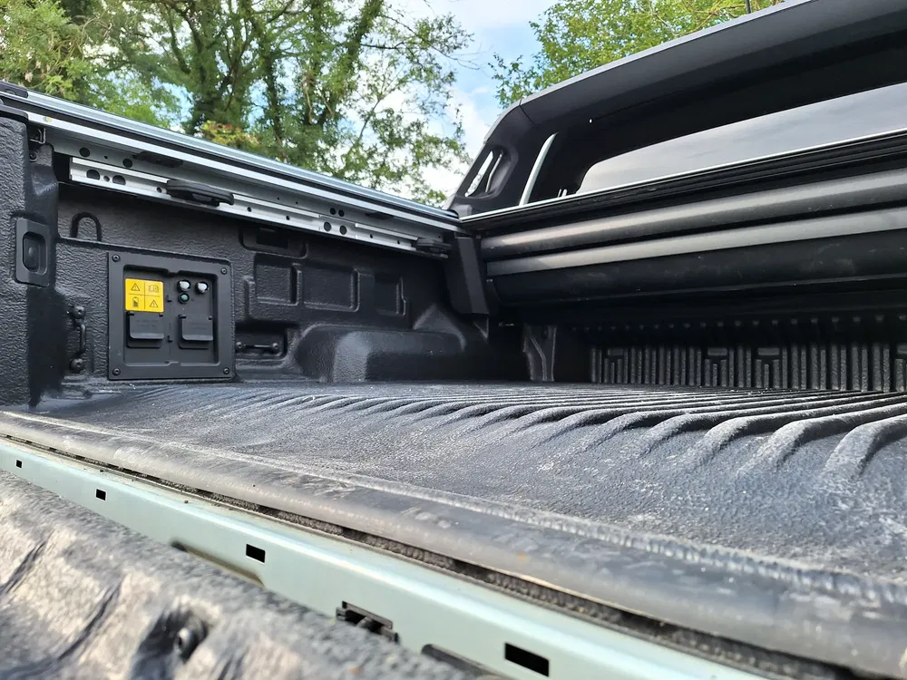 Coffre de pick-up Ford Maverick avec doublure robuste et porte ouverte, arbres en arrière-plan.