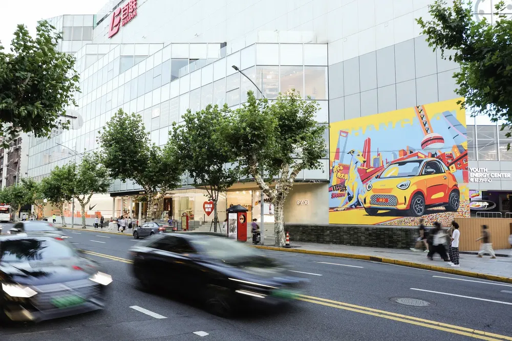 Gevel van winkelcentrum met kleurrijke poster van gele auto op drukke straat.
