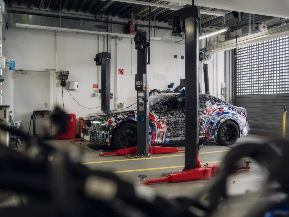 BMW auto prototype met camouflage in een moderne garage met zichtbare werktuigen.