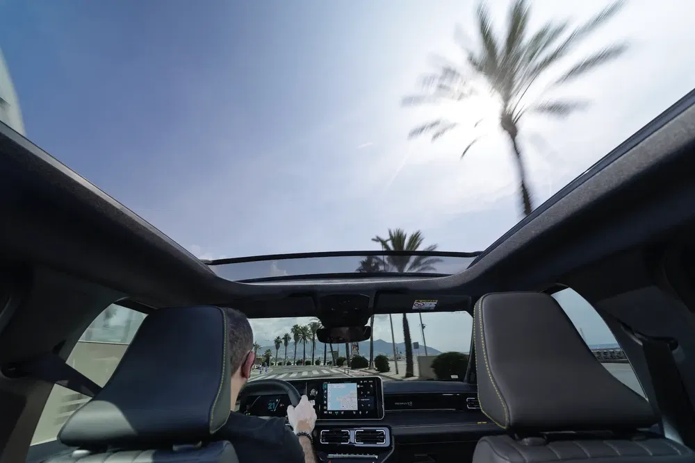 Vue depuis l'intérieur d'une voiture avec toit panoramique, palmiers visibles à l'extérieur.