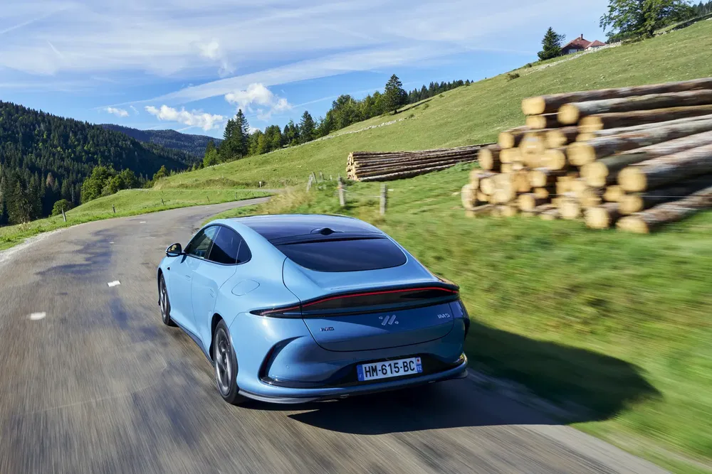 Voiture MG4 électrique bleue sur route de campagne avec paysage verdoyant et ciel bleu.