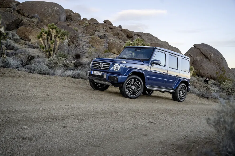 Blauwe Mercedes-Benz G-Klasse in een rotsachtige woestijn met heldere lucht.