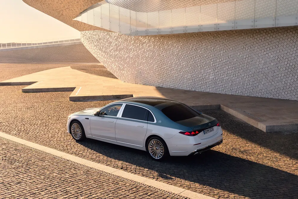 Mercedes-Maybach S-Class blanche garée devant une architecture moderne au coucher du soleil.