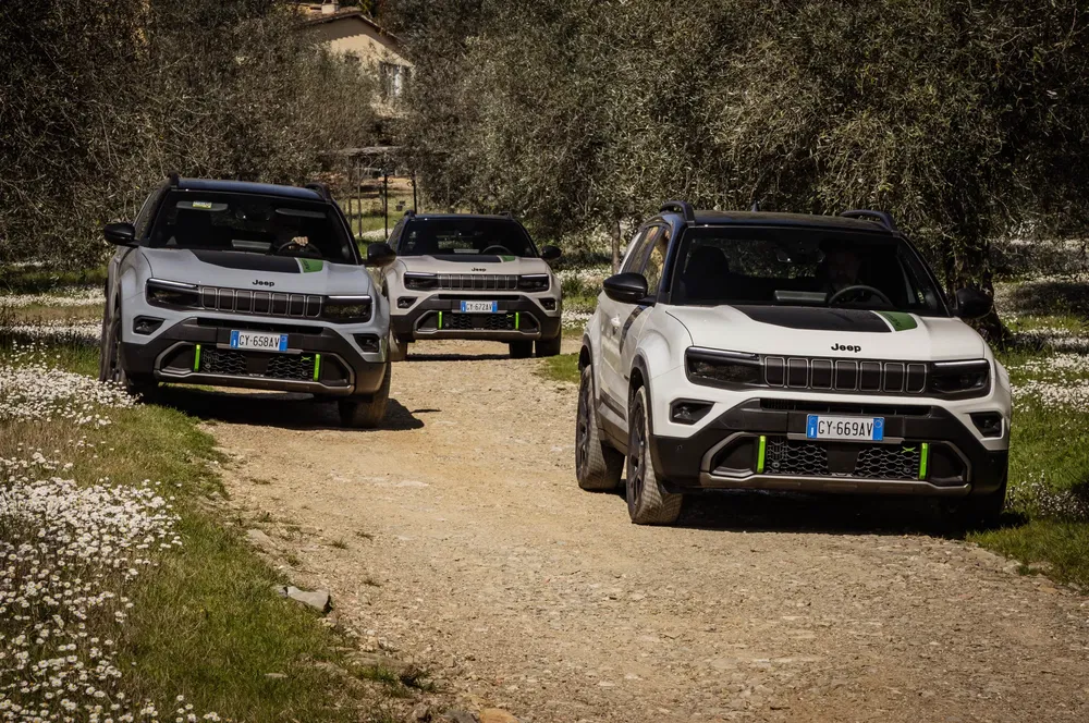 Trois Jeep Compass hybridées roulant sur un chemin terreux entouré par des arbres et fleurs.