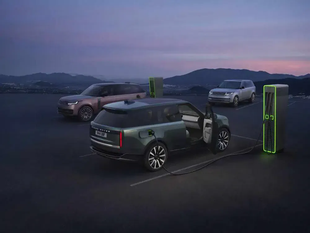 Range Rover électrique se rechargeant sur une station avec vue sur montagnes au crépuscule.