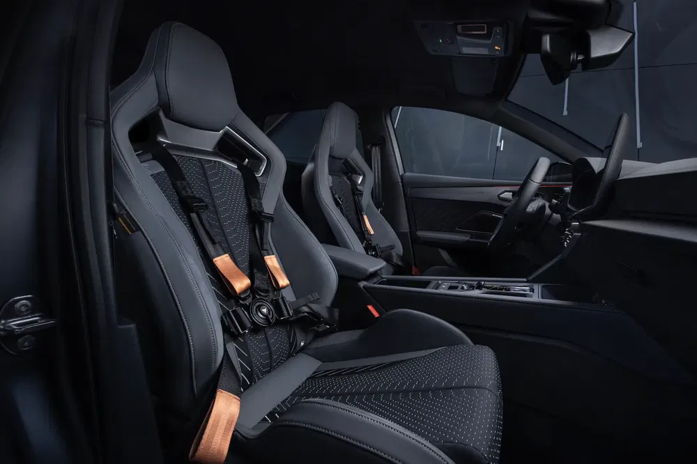Sportief auto-interieur met zwarte kuipstoelen en raceharnassen met koperen details.