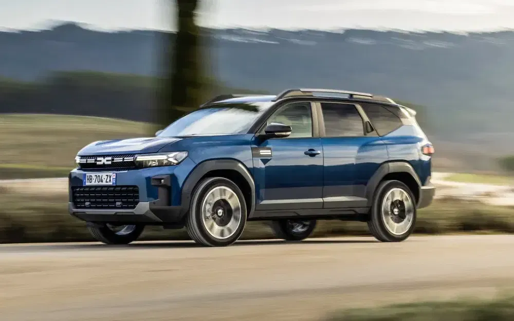 SUV Dacia Duster bleu roulant sur une route de campagne panoramique.