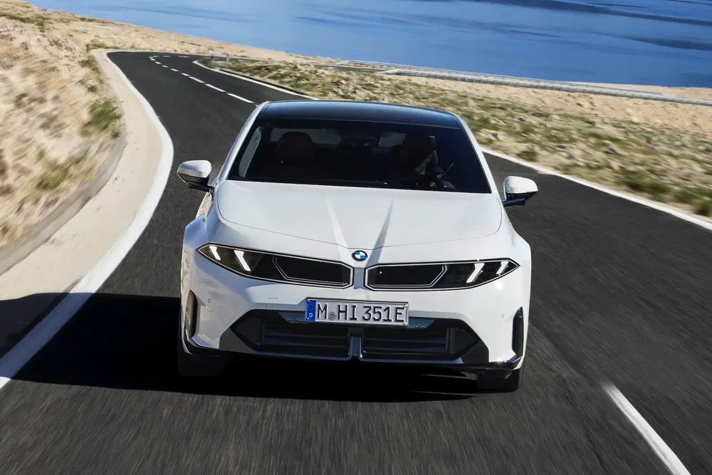 BMW i5 blanche sur route côtière sinueuse, vue avant dynamique.