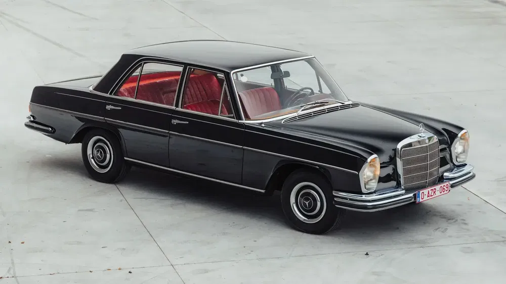 Mercedes-Benz classique noir avec intérieur rouge sur fond en béton.