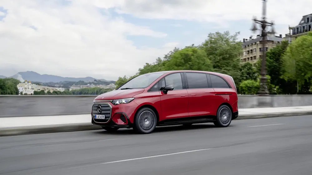 Minivan Mercedes-Benz Classe V rouge roulant sur une route urbaine bordée d'arbres.