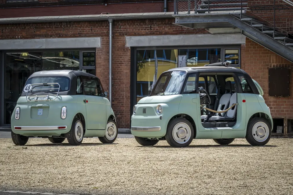 Deux voitures électriques compactes Fiat Topolino vertes garées devant un bâtiment en brique.