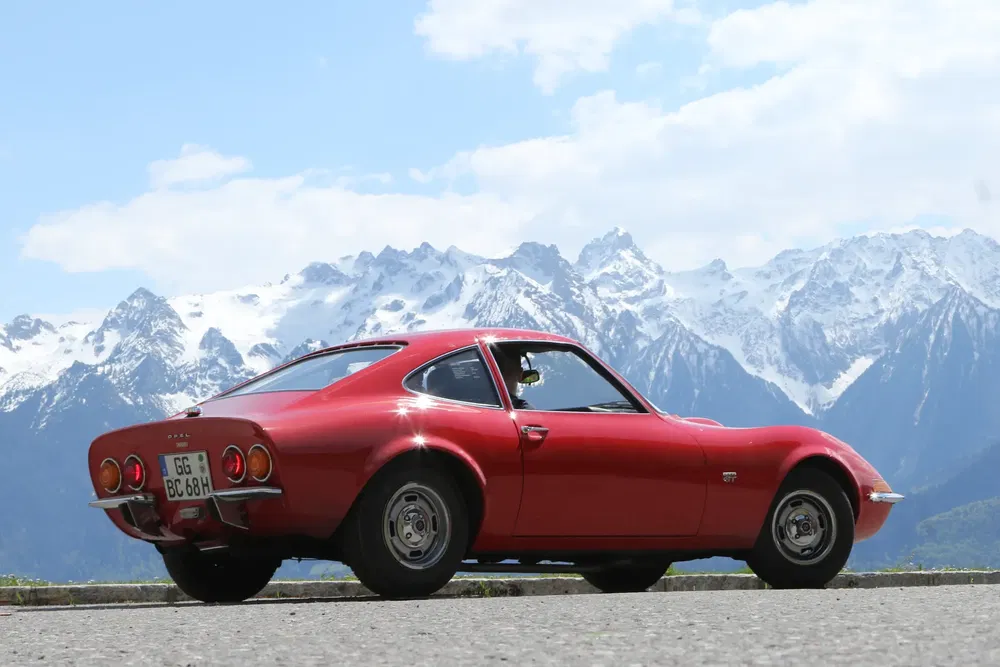 Rode Opel GT voor besneeuwde bergen, heldere blauwe lucht.