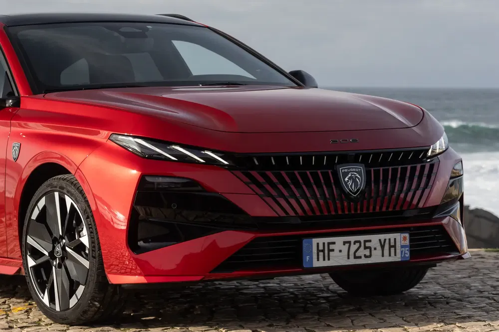 Rode Peugeot 308, modern ontwerp aan zee, opvallende lichtmetalen velgen.