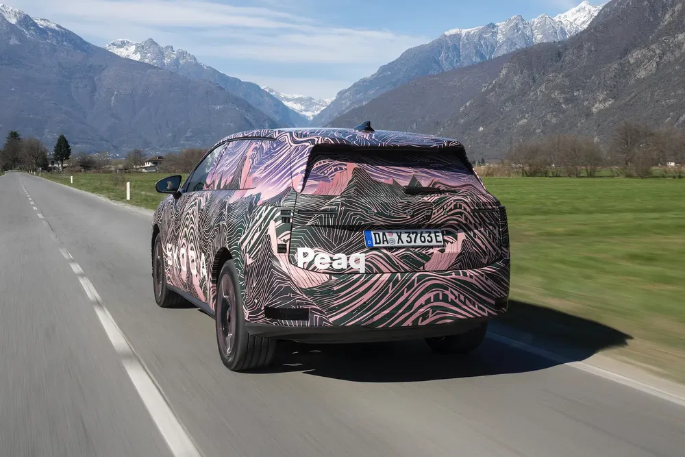 Gecamoufleerde Preeq-auto op een bergweg omgeven door Alpenlandschap.