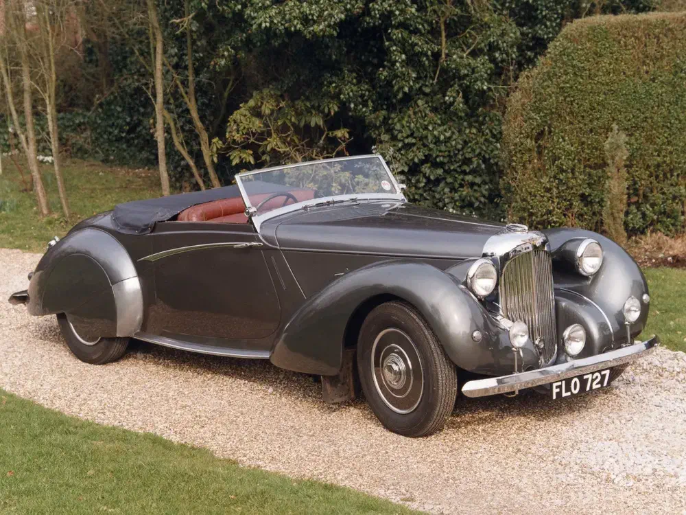 Bentley Mark VI cabriolet classique garé dans une allée de gravier, entouré de verdure.