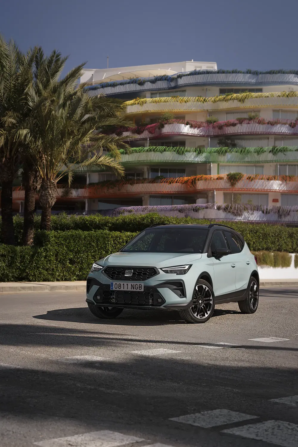 SEAT Arona vert devant un bâtiment coloré et palmiers sous ciel clair.