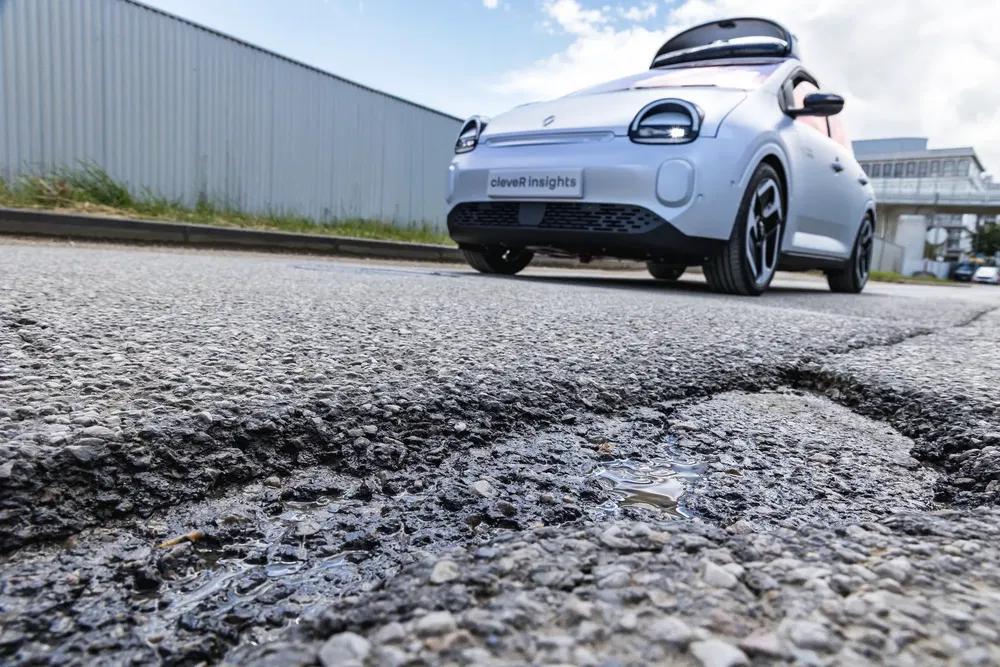 Voiture électrique sur une route avec un nid-de-poule, ciel clair en arrière-plan.