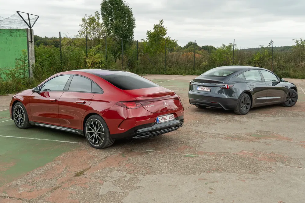 Mercedes CLA rouge et Tesla Model 3 garée sur un terrain bétonné, arrière visible.
