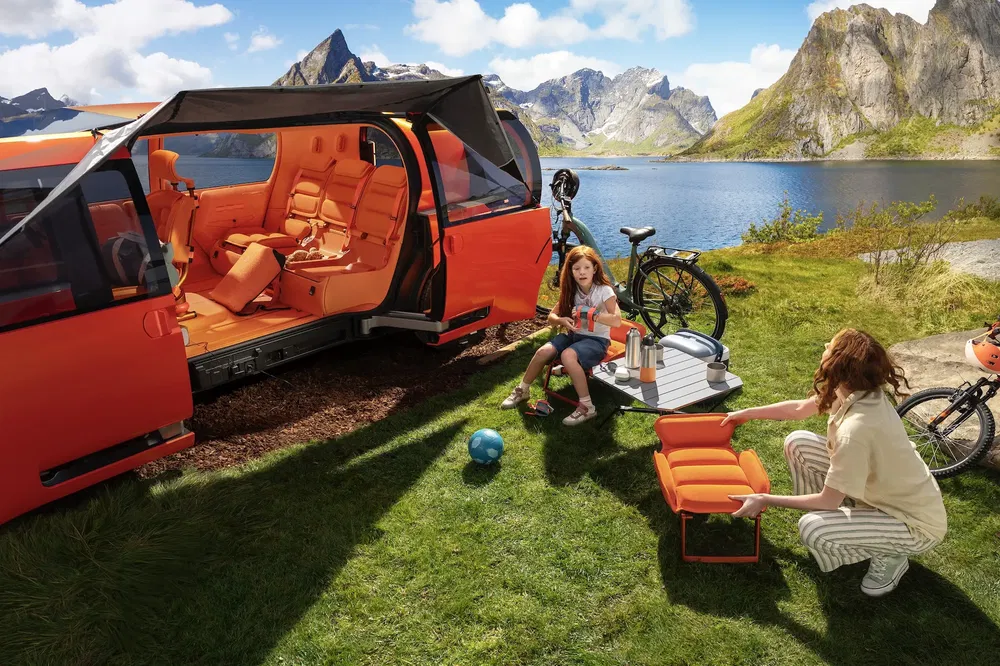 Van orange aménagé pour camping, près d'un lac avec vélos et famille en plein air.