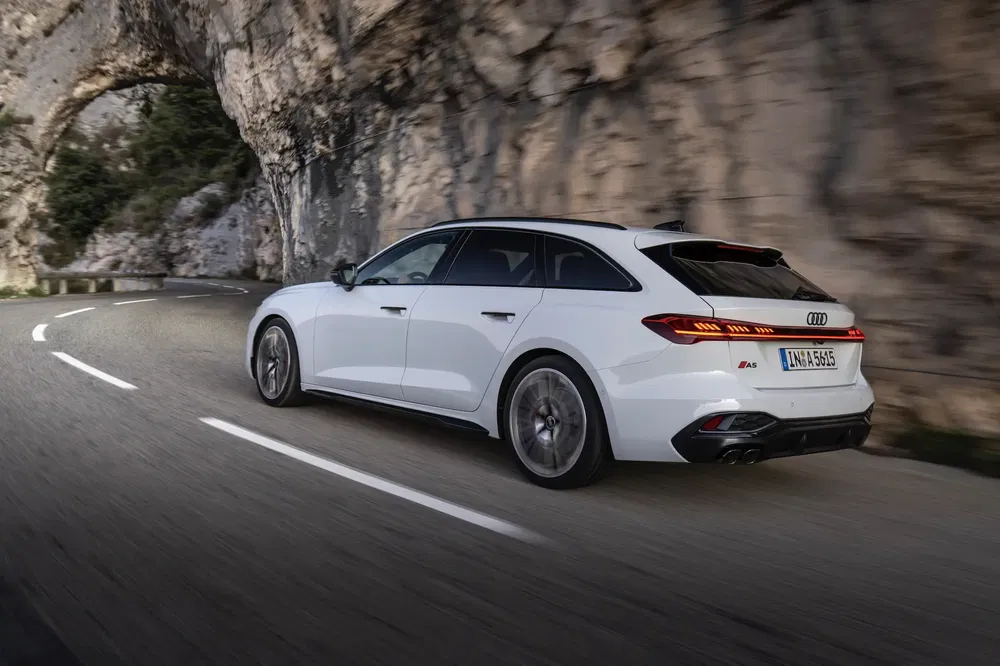Audi A5 Sportback blanche roulant sur route montagneuse, courbe serrée et rochers en arrière-plan.