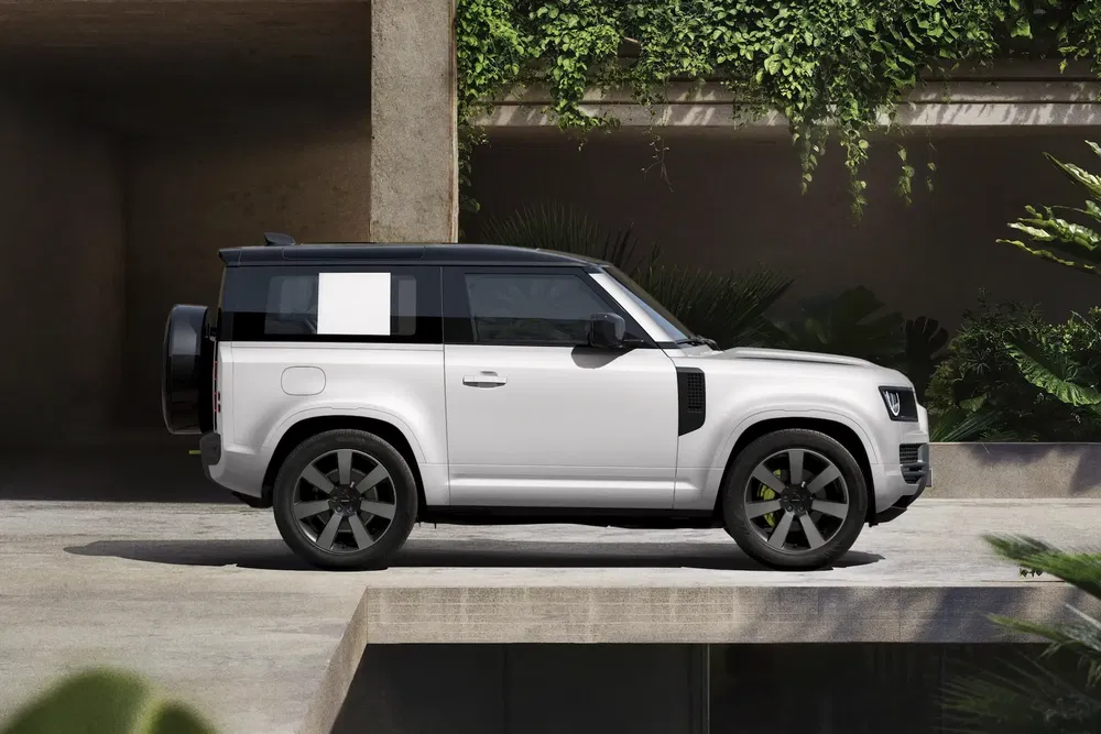 Land Rover Defender blanc moderne, stationné dans un cadre architectural avec verdure luxuriante.