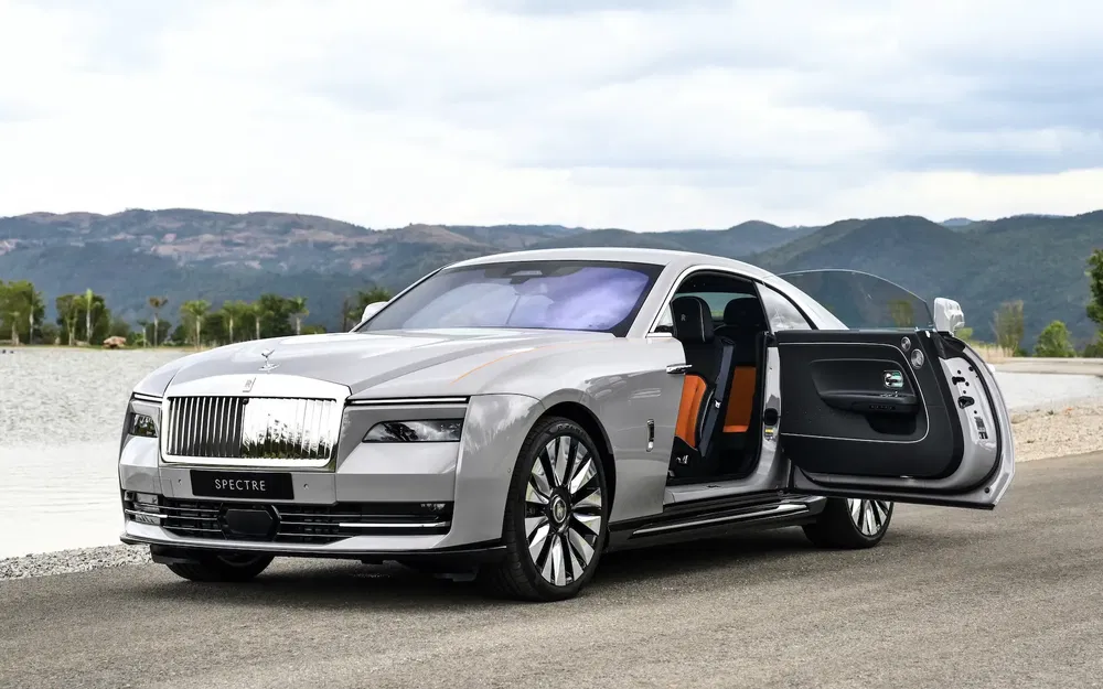 Rolls-Royce Spectre grise avec portière ouverte devant un lac pittoresque.