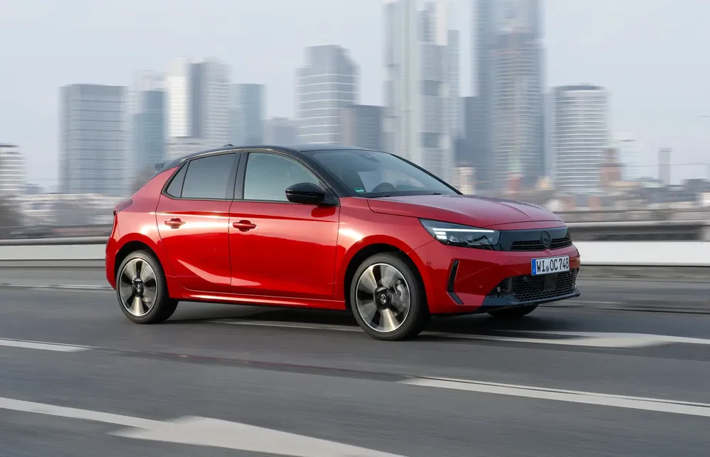 Opel Corsa rouge roulant sur une autoroute urbaine avec skyline en arrière-plan.